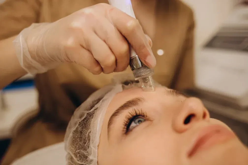 Una persona recibe un tratamiento facial con un dispositivo en la frente, en un salón.