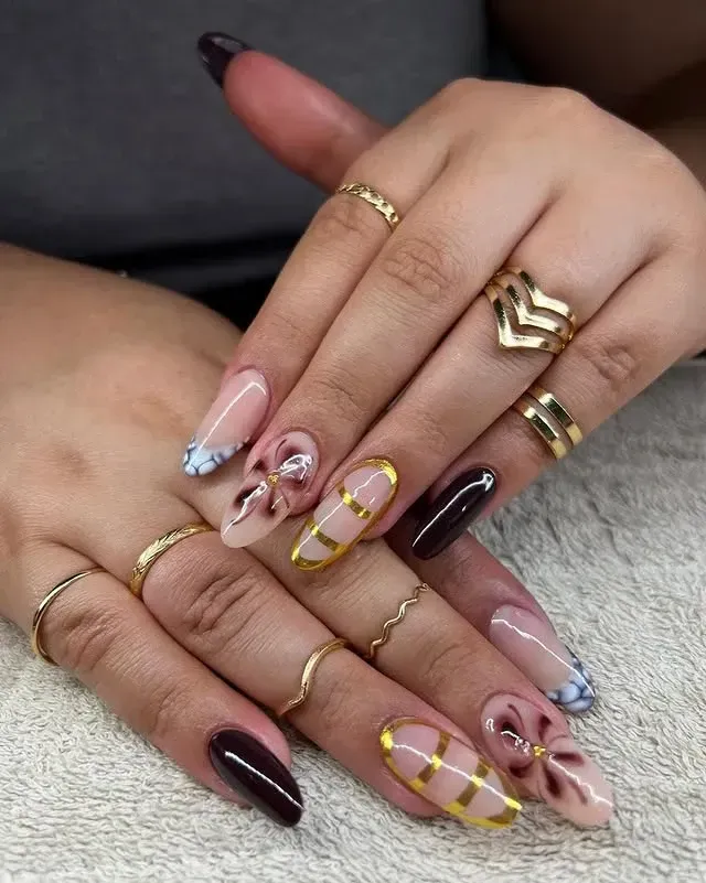 Manos con variedad de anillos dorados y diseños de uñas largas y ovaladas
