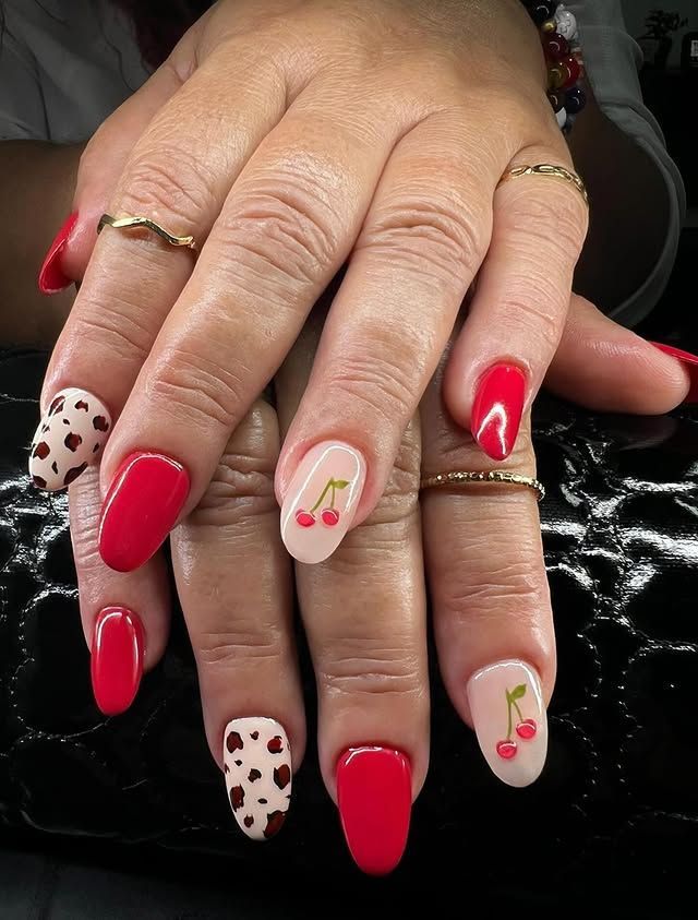 Uñas rojas y con estampado de corazones con acento de cereza sobre un fondo negro.