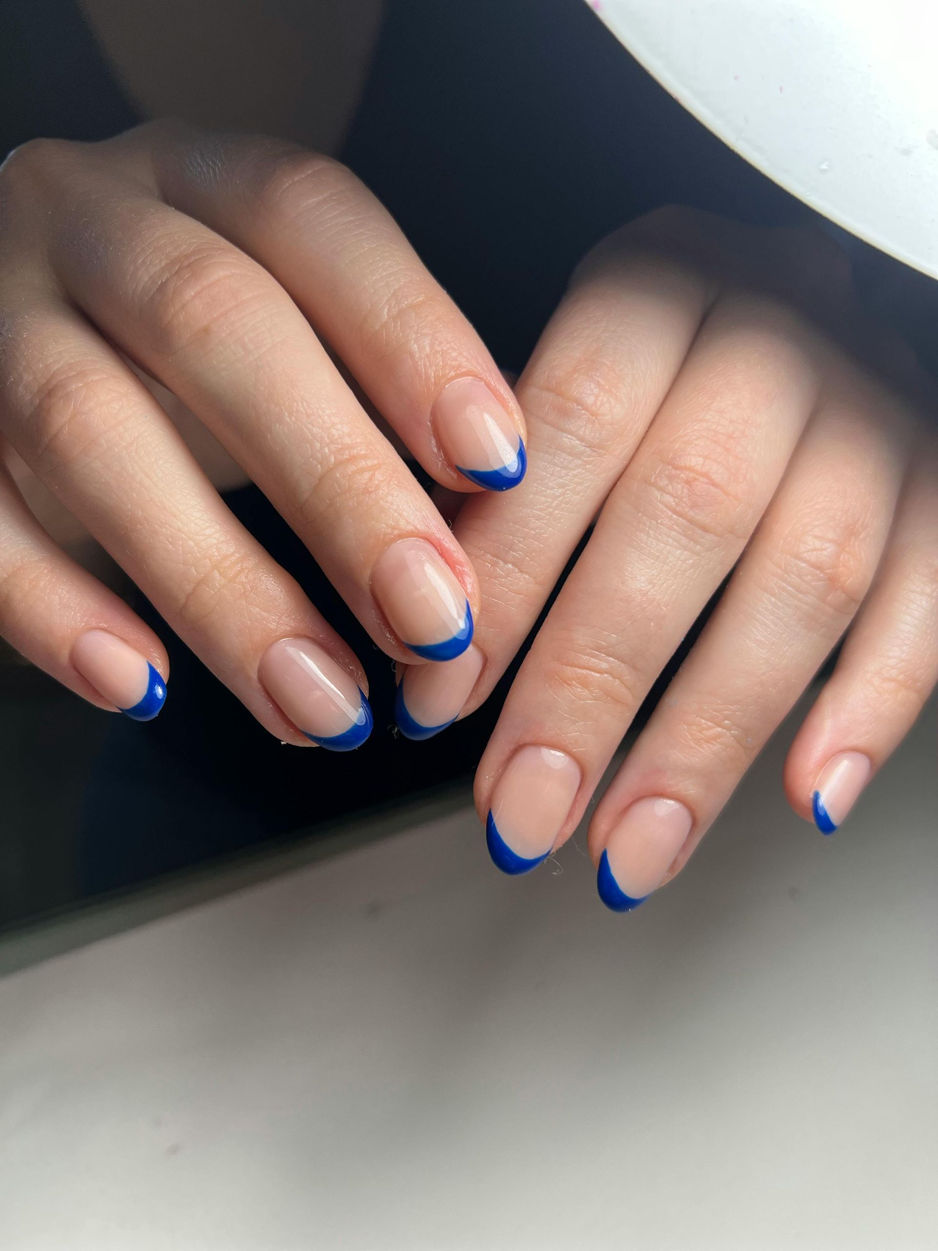 Manos con uñas cortas y color piel que presentan una punta francesa en un vibrante color azul.