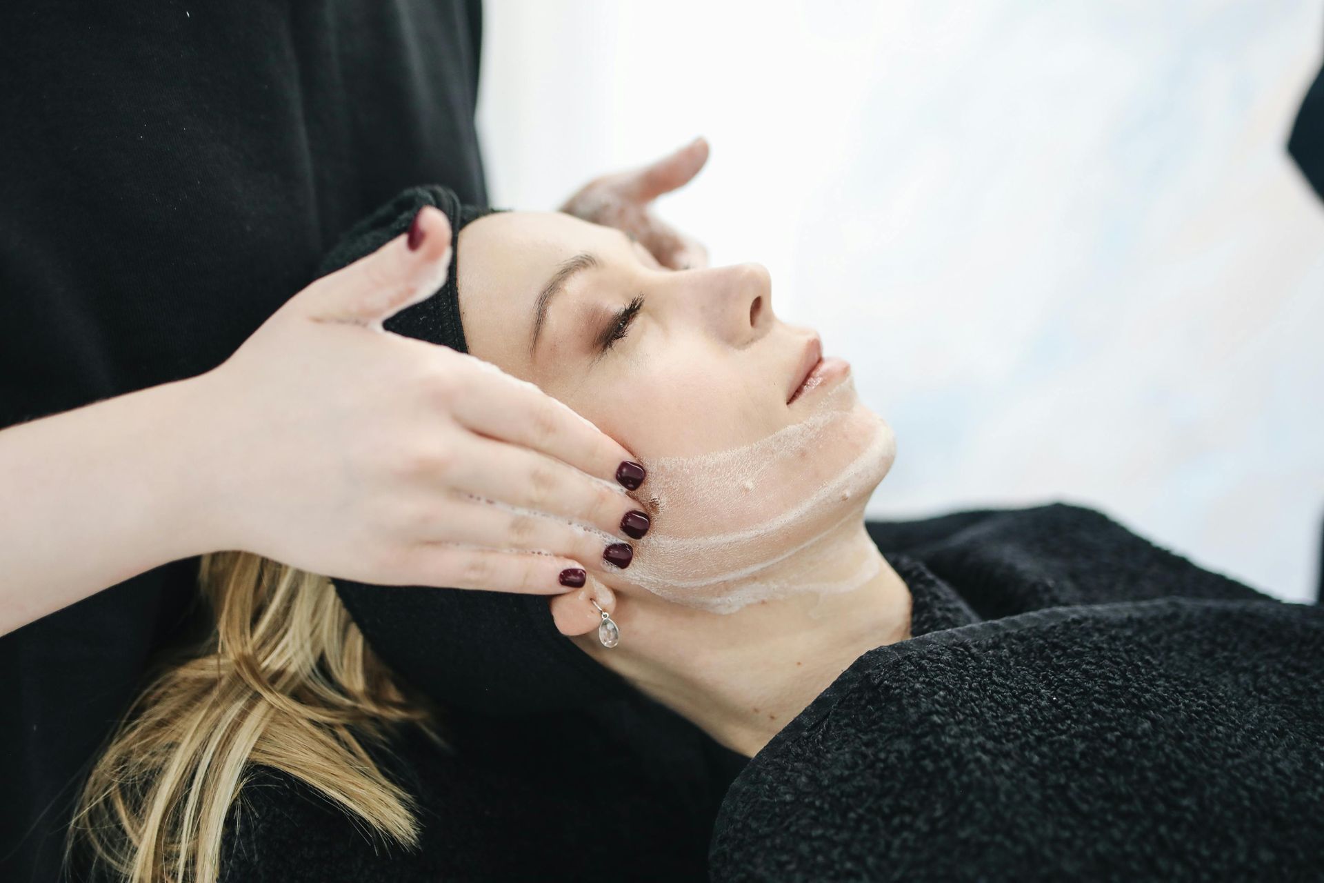 Mujer recibiendo tratamiento facial; entorno de spa, manos masajeando la cara con el producto.