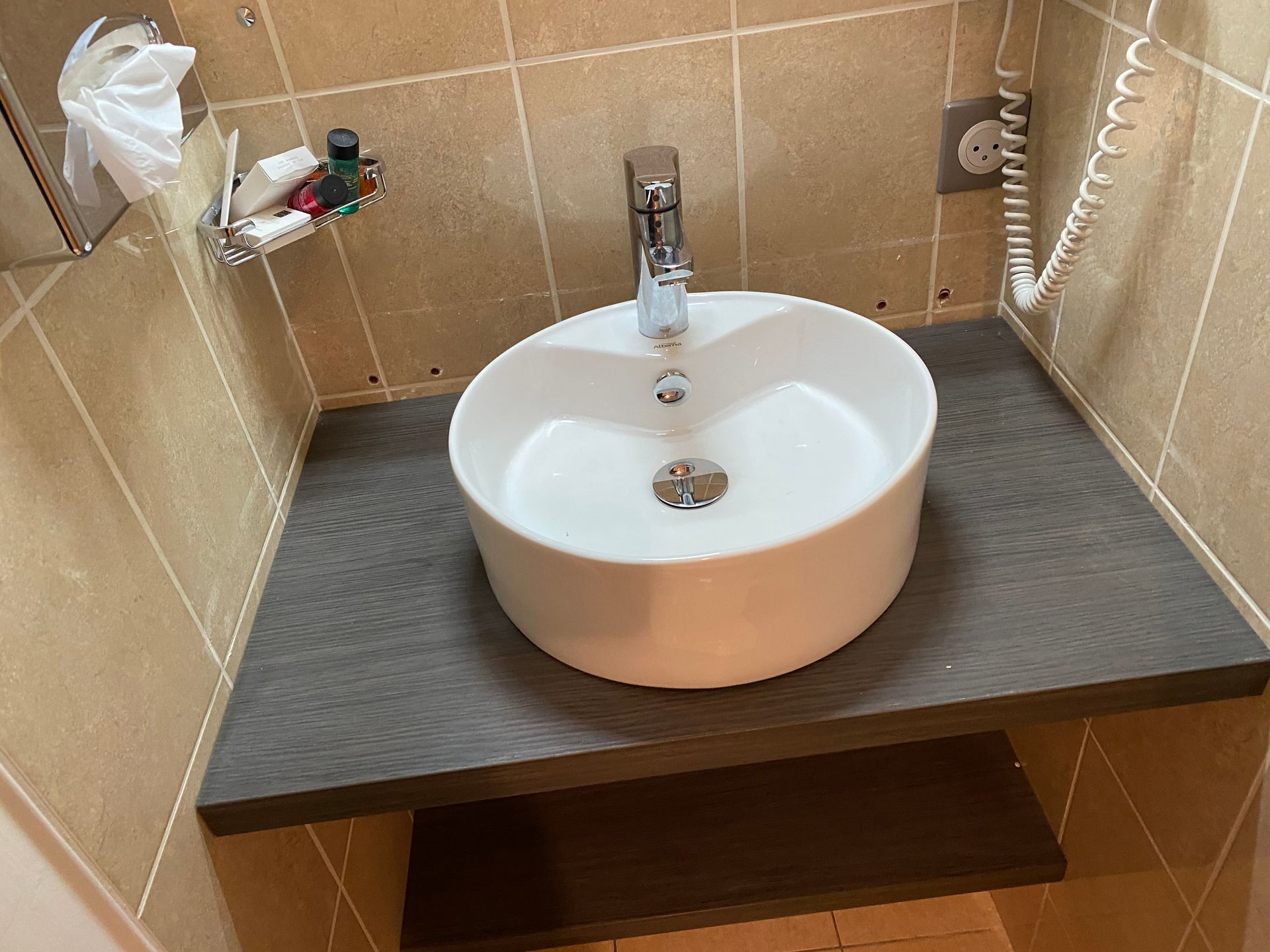 Lavabo rond blanc sur un comptoir foncé, devant des carreaux beiges.