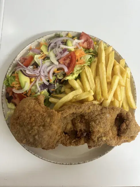 Un plato de comida con patatas fritas y una ensalada en una mesa.