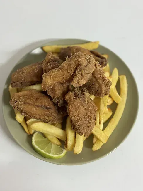 Un plato de alitas de pollo fritas y papas fritas en una mesa.