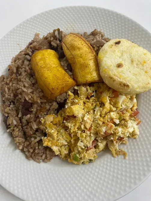 Un plato blanco cubierto con arroz, huevos, plátanos y pan.
