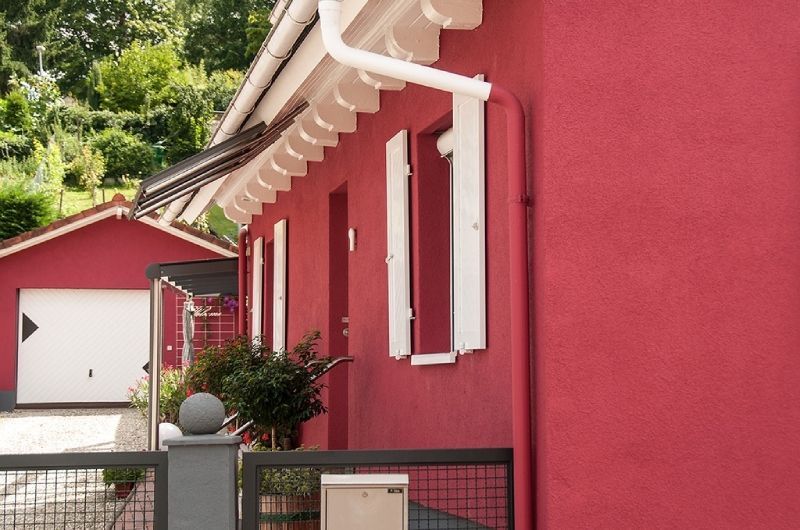Rotes Haus mit weißen Fensterläden, Markise und einer Garage im Hintergrund