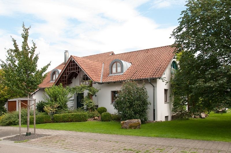 Weißes Haus mit rotem Ziegeldach und grünem Garten in einer ruhigen Straße