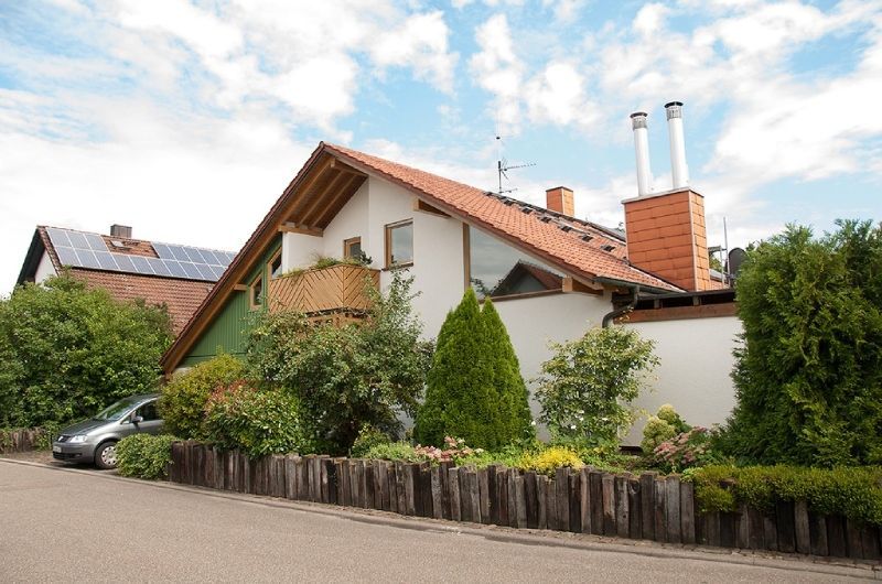 Einfamilienhaus mit rotem Ziegeldach, Schornstein und üppigem Vorgarten an einer ruhigen Straße