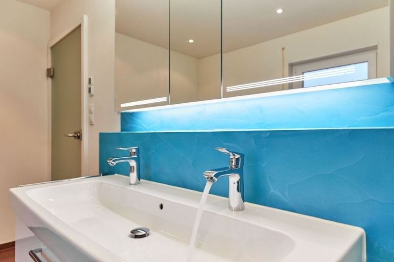 Modernes Badezimmerwaschbecken mit zwei Armaturen, Spiegel und blauer Rückwandbeleuchtung
