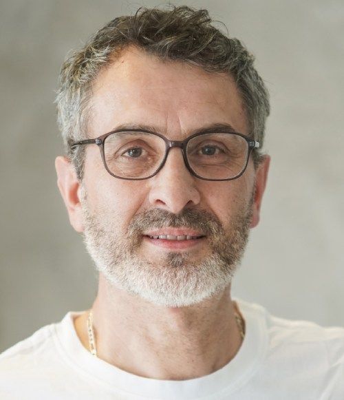 Porträt eines lächelnden Mannes mit Brille, kurzem grauen Haar und weißem Hemd vor neutralem Hintergrund