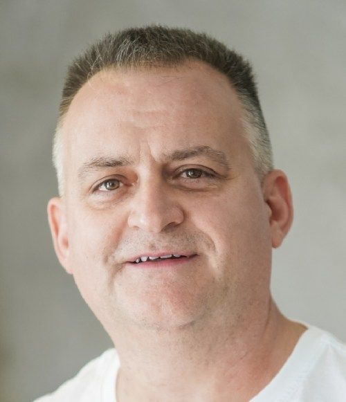 Porträt eines lächelnden Mannes in einem weißen Hemd vor hellem Hintergrund