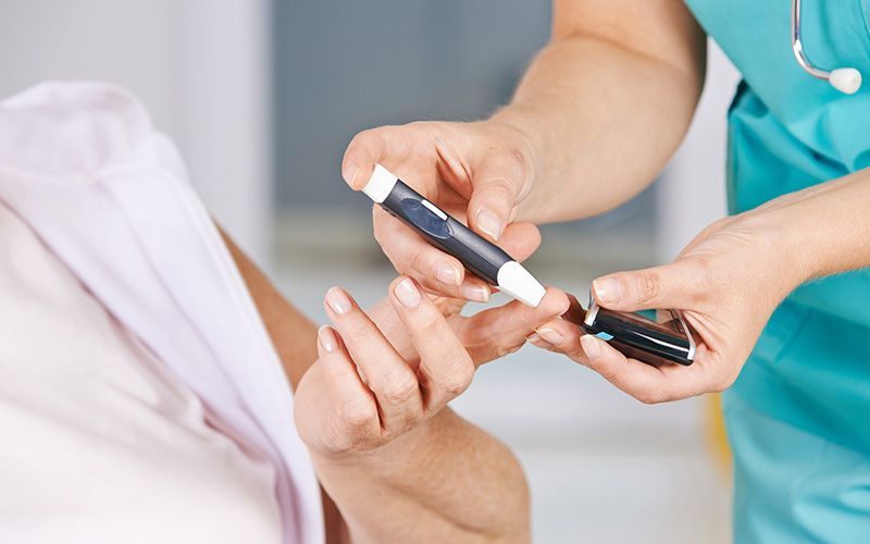 Pflegerin entnimmt Blut von einer Patientin um den Blutzucker zu messen.