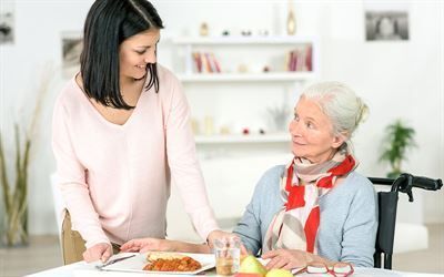 Eine Frau serviert einer älteren Frau im Rollstuhl Essen.