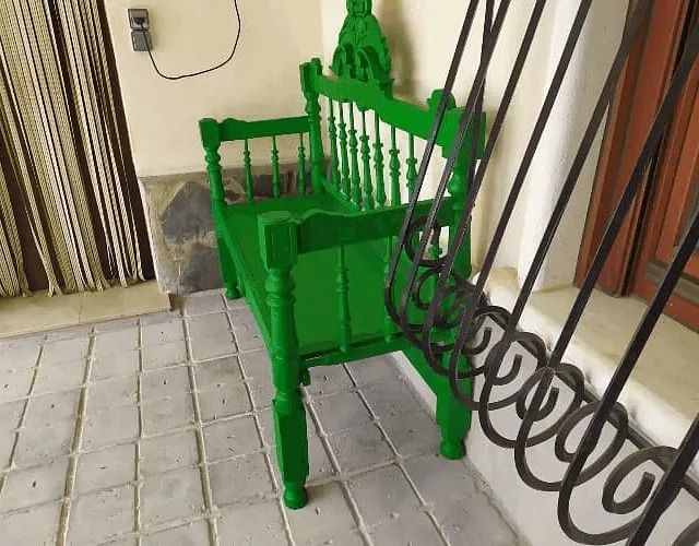 Un banco verde está sentado en un porche al lado de una valla de hierro forjado.