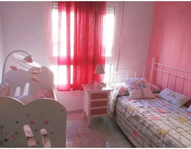 Un dormitorio con paredes rosas, una cama y una cuna.