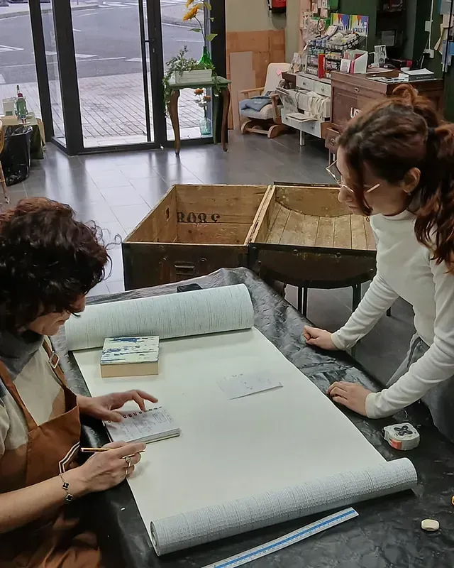 Dos mujeres están sentadas en una mesa midiendo un trozo de papel.