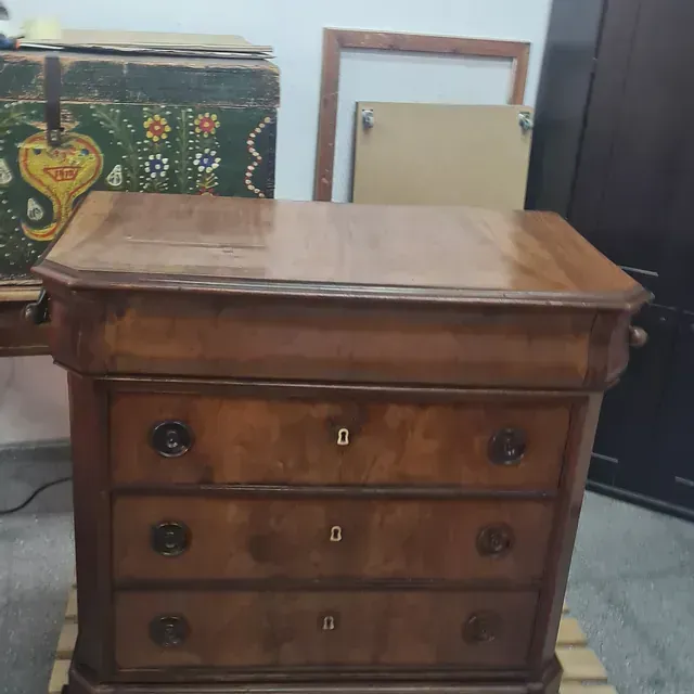 Una cómoda de madera con un baúl verde al fondo