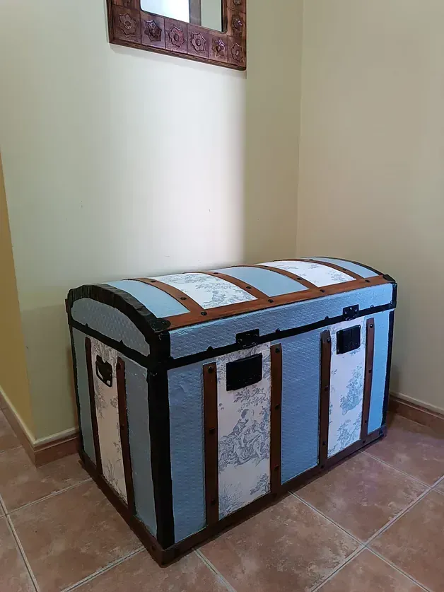 Un baúl azul y marrón está en un pasillo al lado de un espejo.