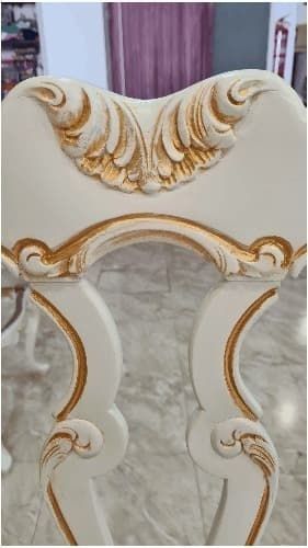 Una silla blanca con tallas doradas reposa sobre un piso de baldosas.