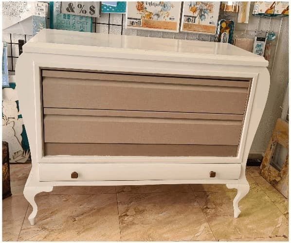 Una cómoda blanca con cajones marrones se encuentra sobre un suelo de baldosas.