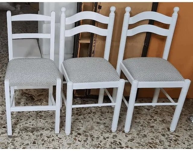 Tres sillas blancas están alineadas sobre un suelo de baldosas.