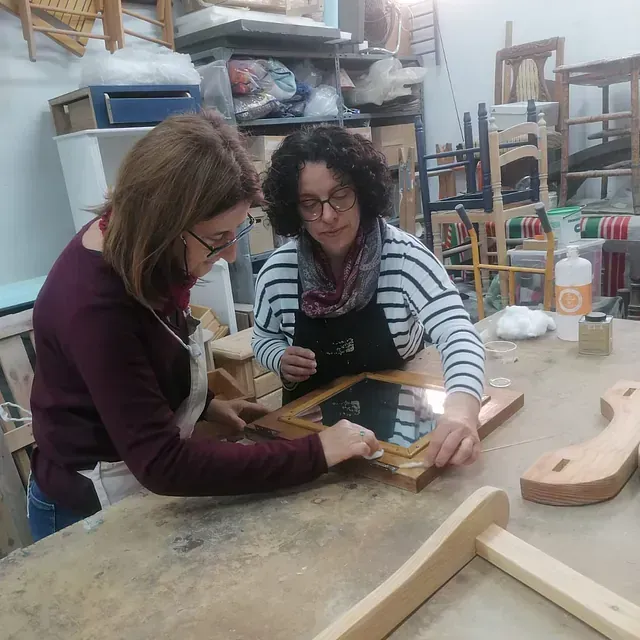 Dos mujeres están sentadas en una mesa trabajando en un trozo de madera.