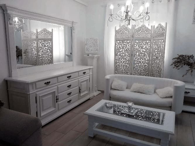 Una sala de estar con un sofá blanco, una cómoda, una mesa de café y un espejo.