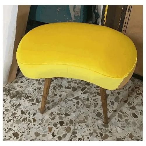 Un taburete amarillo con patas de madera está sobre un suelo de baldosas.