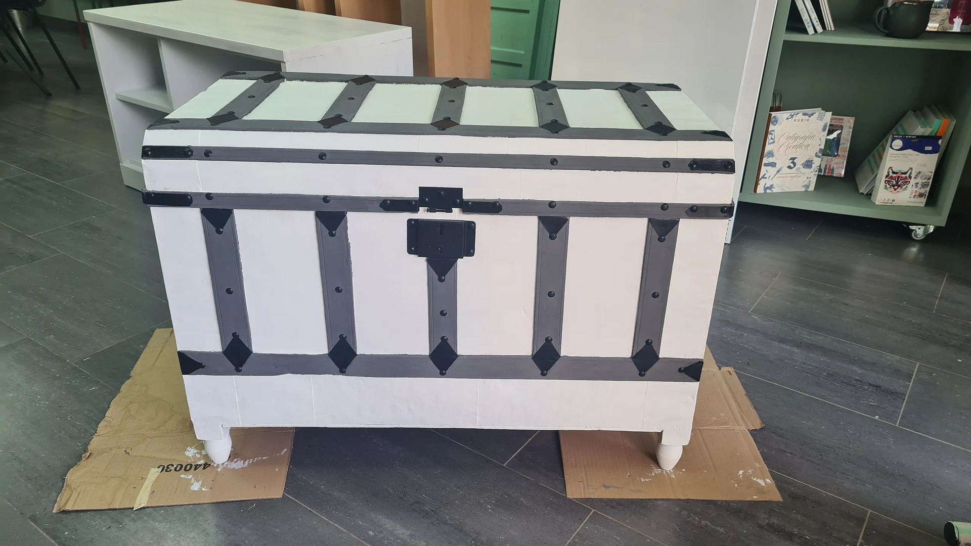 Un baúl blanco y negro reposa sobre un trozo de cartón.