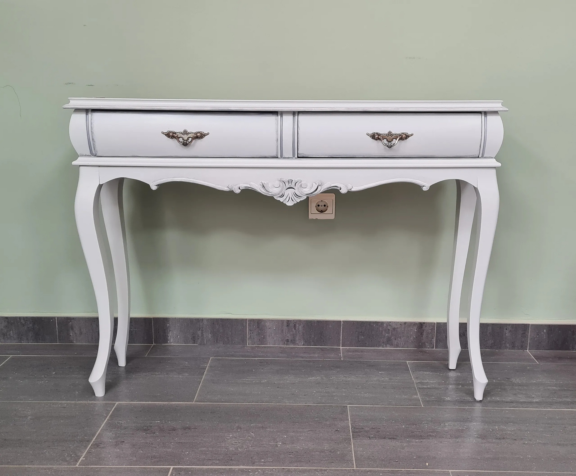 Una mesa blanca con dos cajones está contra una pared verde.