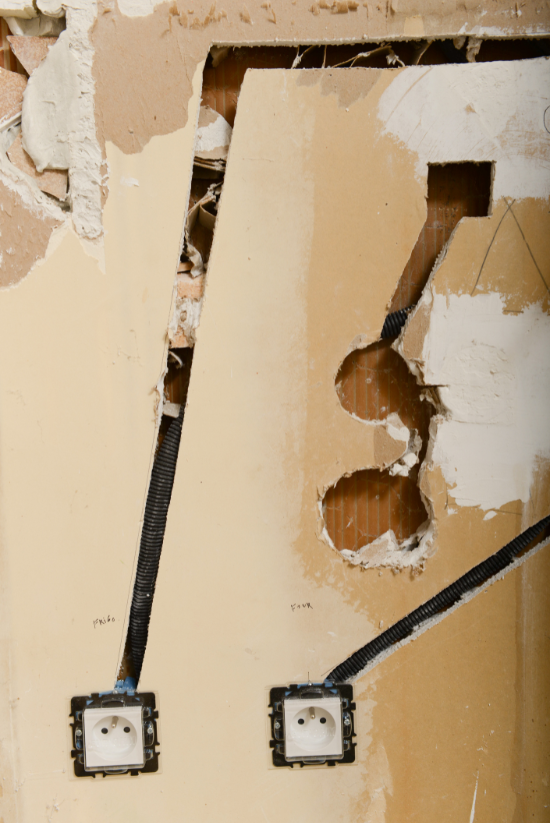 Prises et câblage apparents dans un mur lors d'une rénovation. Plâtre beige et composants électriques visibles.