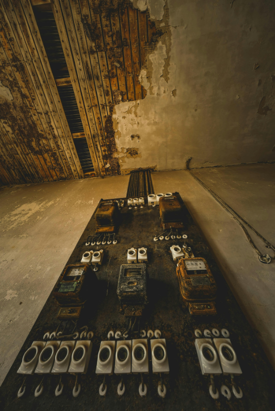 Vieux panneau de commande électrique patiné sur un mur dans une pièce en ruine.