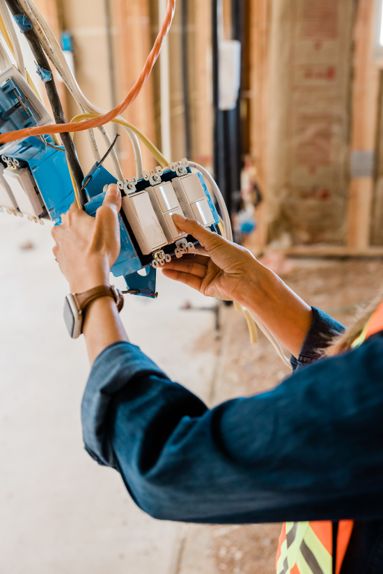 Électricien installant des interrupteurs d'éclairage dans un bâtiment partiellement construit.