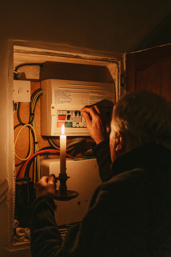 Un homme utilise une bougie pour vérifier une boîte à fusibles dans une pièce sombre.