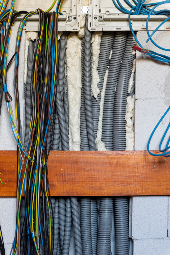 Câblage électrique en faisceaux de conduits gris, avec des fils colorés et une poutre en bois dans un mur.