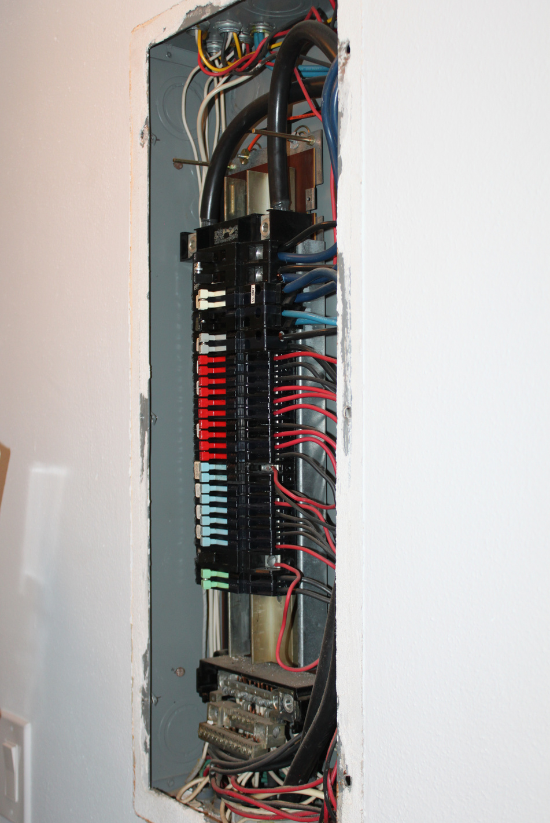 Panneau électrique avec plusieurs disjoncteurs et fils exposés dans un mur.