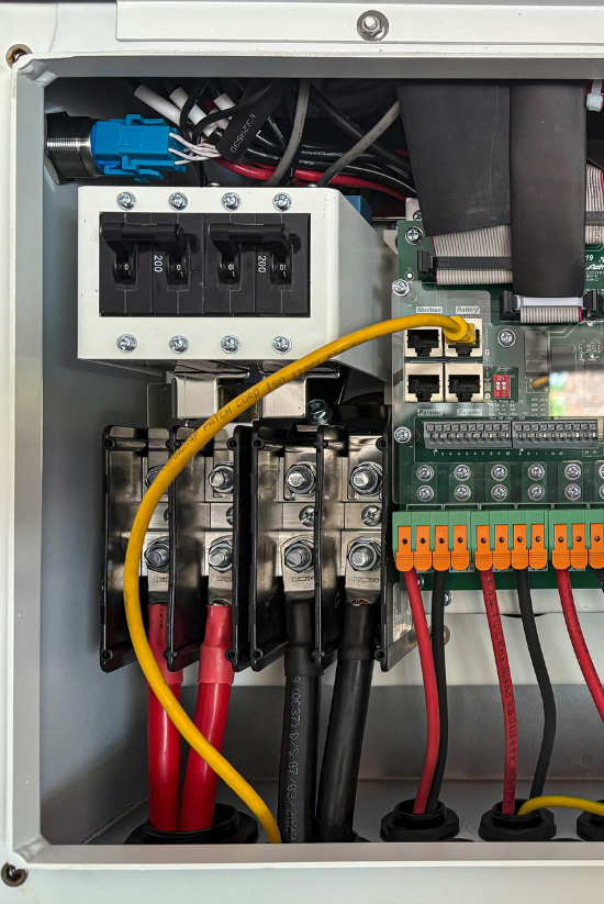 À l'intérieur d'un boîtier métallique blanc, câblage électrique : câbles noirs.