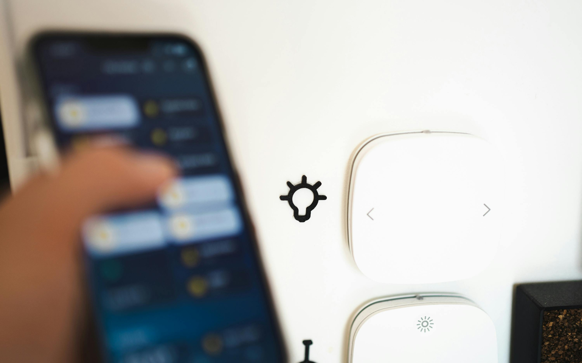 Une personne tenant un téléphone contrôle des appareils intelligents sur un mur blanc.