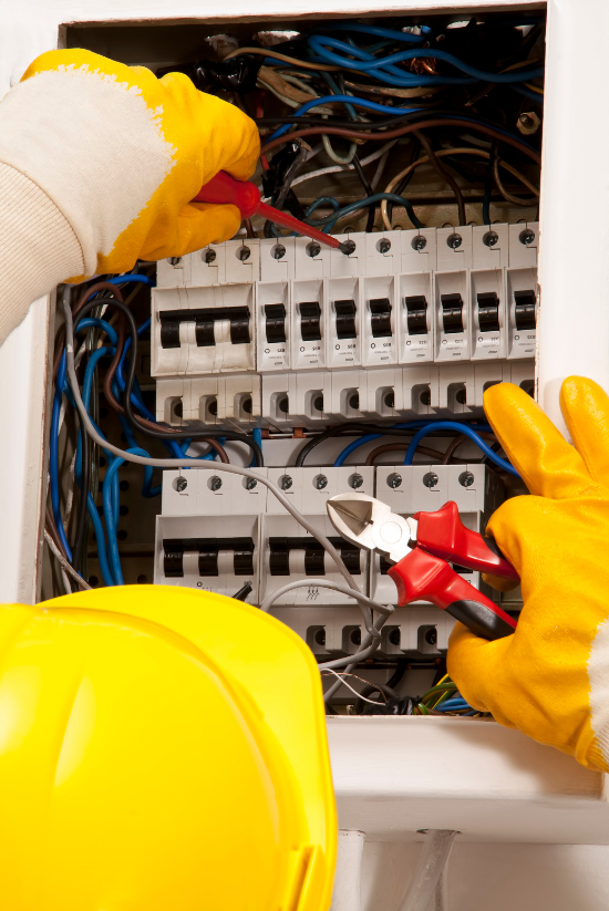 Électricien travaillant à l'intérieur d'un panneau électrique, portant des gants jaunes.