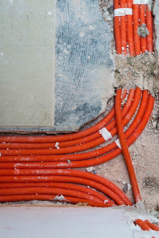 Tubes de conduits électriques orange dans un mur, ruban blanc, chantier de construction.