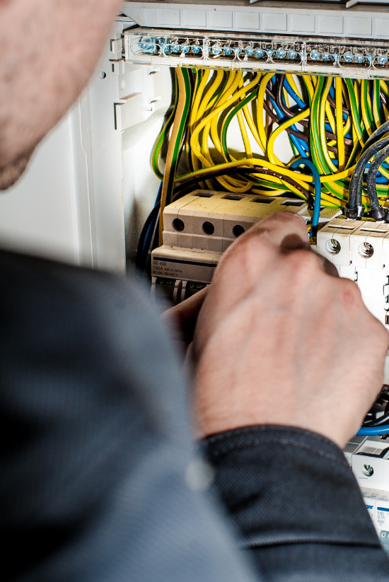 Électricien travaillant à l'intérieur d'un panneau électrique, entouré de fils jaunes et verts.