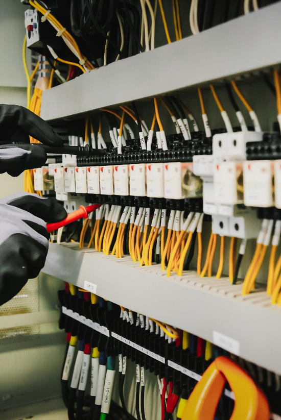 Mains portant des gants travaillant sur le câblage électrique d'un panneau.