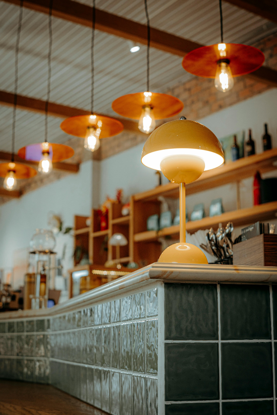 Une lampe de bureau jaune et des suspensions éclairent un comptoir de café.