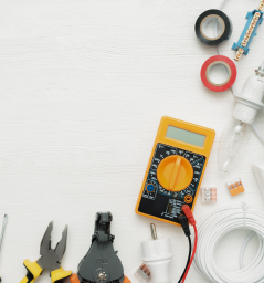 Outils et composants électriques sur fond blanc, notamment un multimètre, une pince, un fil et du ruban adhésif.