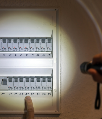 Une personne éclaire avec une lampe de poche un boîtier de disjoncteur, pointant vers un interrupteur numéroté.