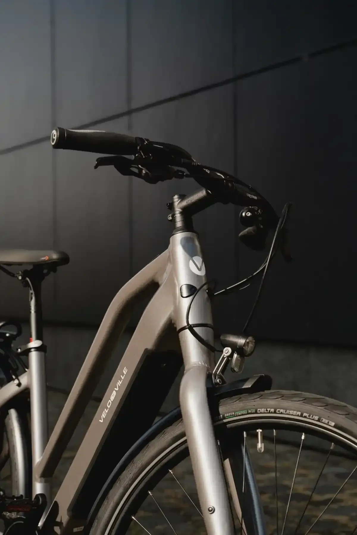 Bicicleta plateada con manillar negro sobre un fondo de pared oscura.