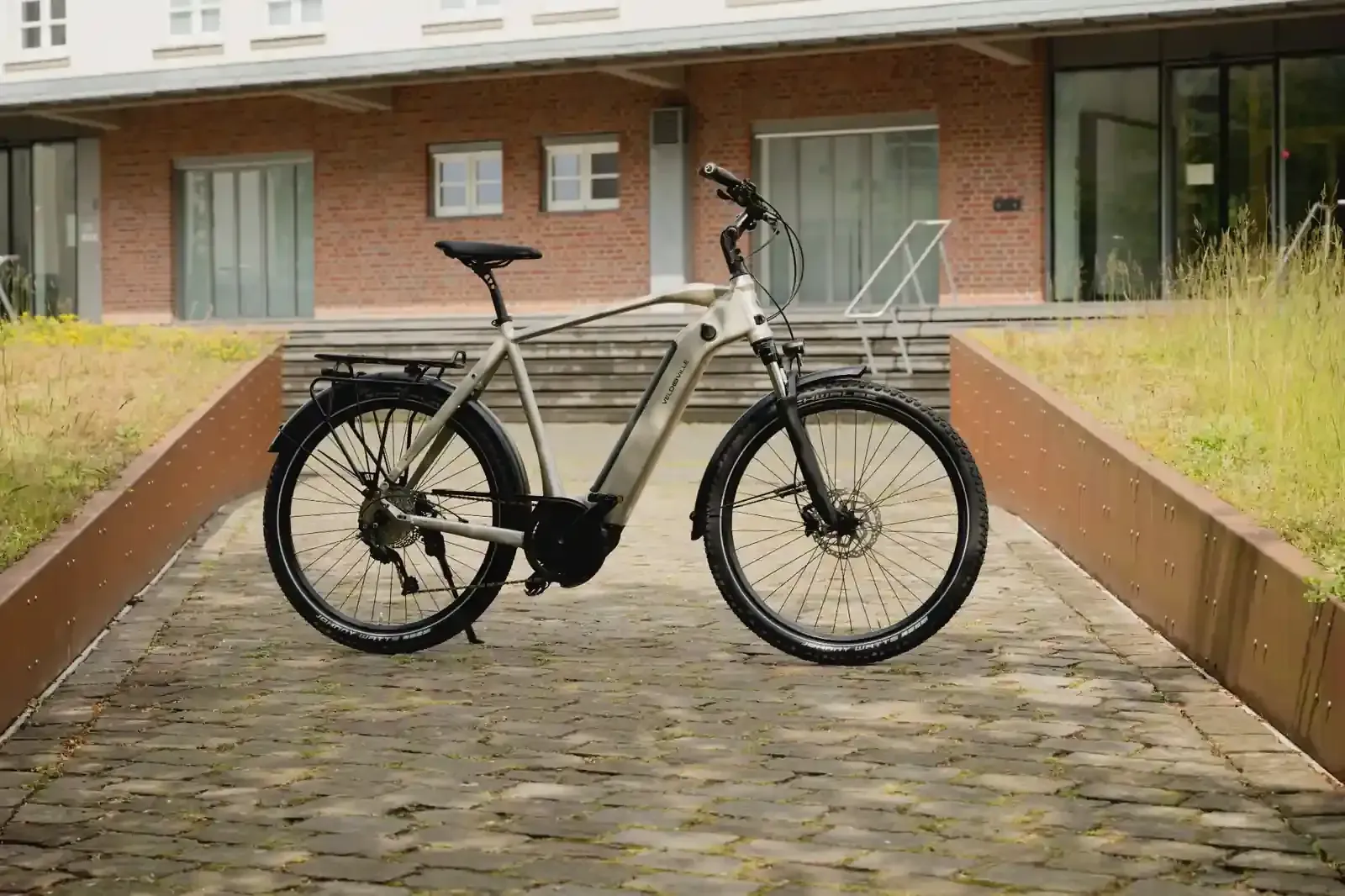 Bicicleta eléctrica negra en un camino empedrado frente a un edificio de ladrillos.