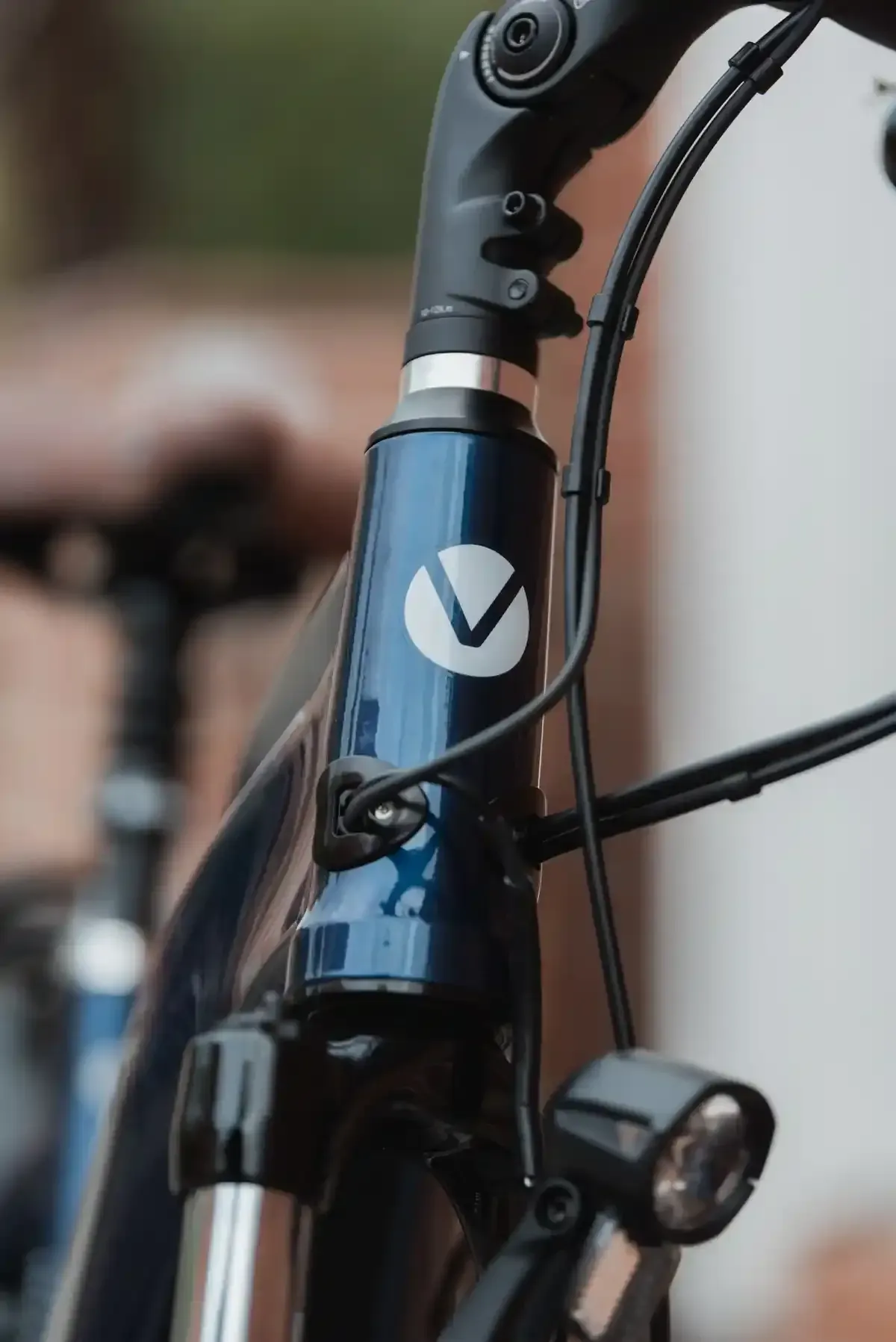 Primer plano del tubo de dirección y el manillar de una bicicleta azul con un logotipo en forma de V blanca.