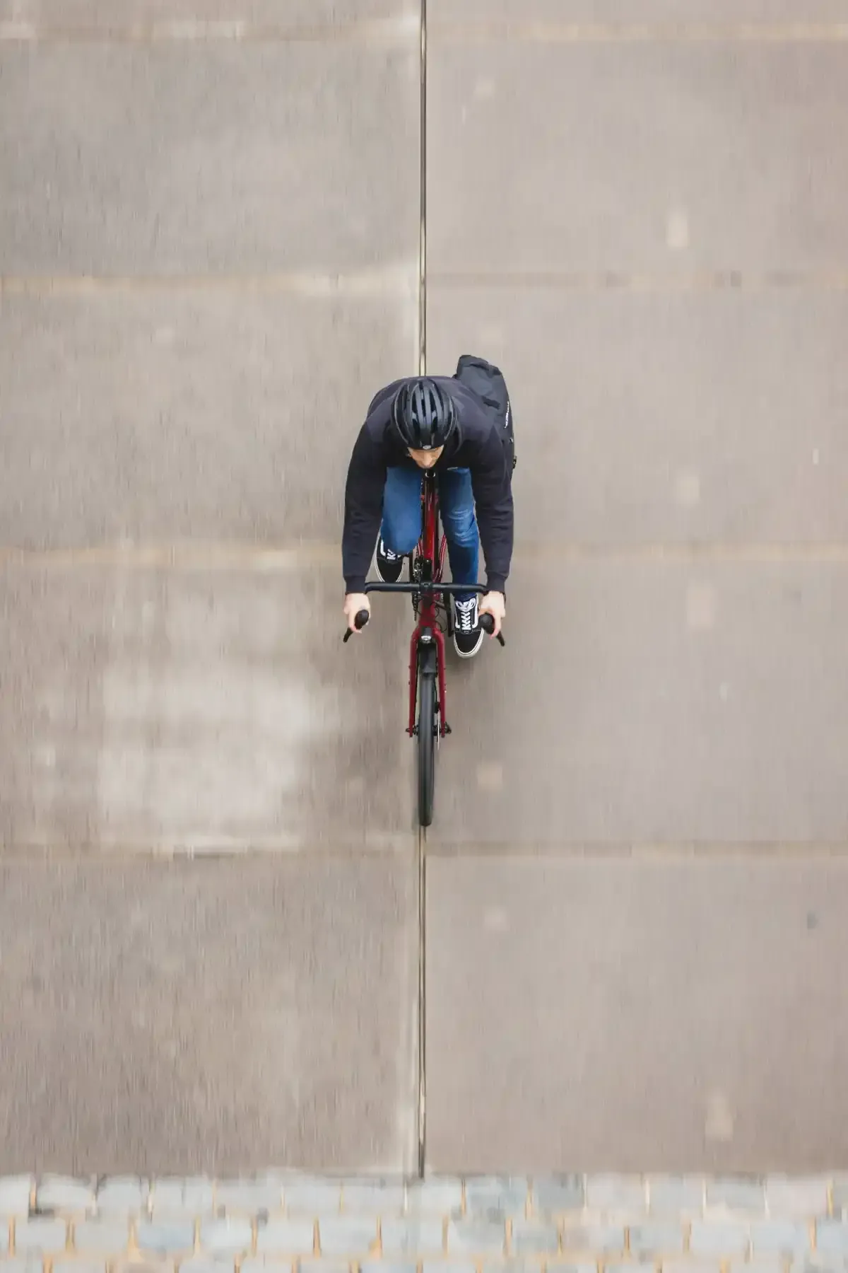 Ciclista con ropa oscura montando una bicicleta roja sobre un pavimento gris.