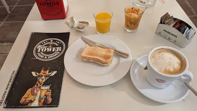 Desayuno: tostadas, zumo de naranja, capuchino, fruta y sobres de azúcar en una mesa de café.